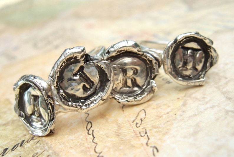 May include: Three silver rings with raised letters, J, R, and H, set in a wax seal design.