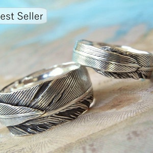 May include: Two silver rings with a feather design. The rings are stacked on top of each other.