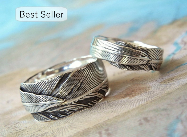 May include: Two silver rings with a feather design. The rings are stacked on top of each other.