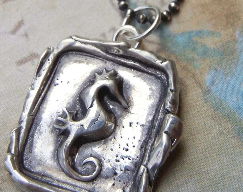 May include: Silver pendant necklace featuring a detailed, three-dimensional seahorse design. The pendant is square-shaped with a textured, aged finish.
