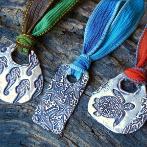 May include: Three silver pendants with different designs: a seahorse, a starfish, and a turtle. Each pendant is attached to a colorful ribbon.