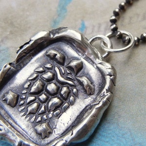 May include: A silver necklace with a pendant featuring a detailed turtle design. The pendant is textured and has a rustic, antique look.