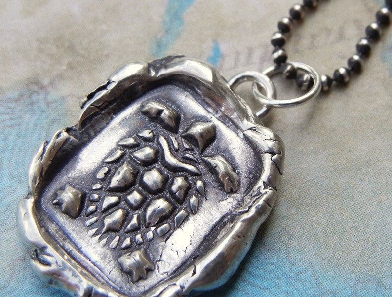 May include: A silver necklace with a pendant featuring a detailed turtle design. The pendant is textured and has a rustic, antique look.