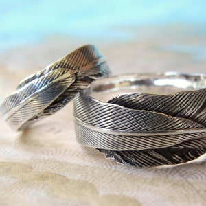 May include: Two silver rings with a feather design. The rings are stacked on top of each other.
