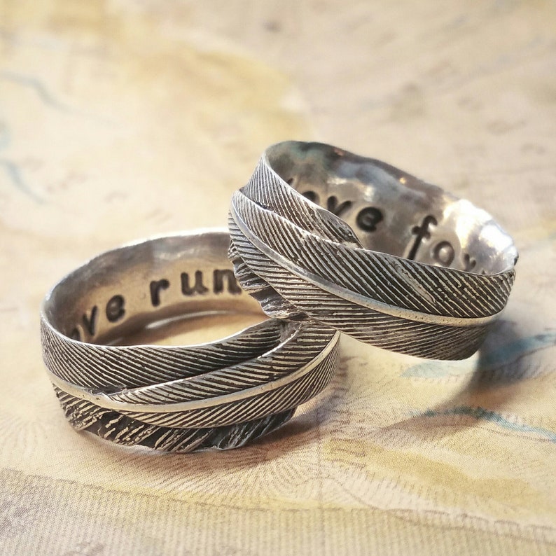 May include: Two silver rings with a feather design. The rings are engraved with the words "we run" and "we fly".