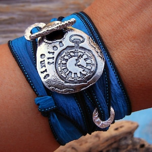 May include: A blue and black silk ribbon bracelet with a silver charm featuring a clock face and the words "Always" and "Emily".