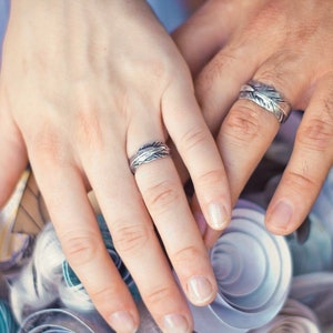 May include: A close-up of two hands with silver wedding bands. The bands have a unique, intricate design.