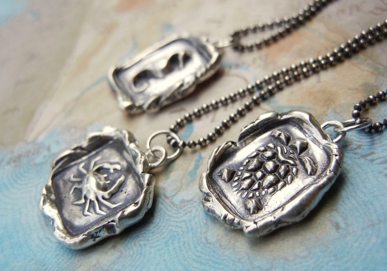 May include: Three silver pendants on chains, each featuring a different design: a crab, a turtle, and a seahorse. The pendants are detailed and have a textured, antique finish.