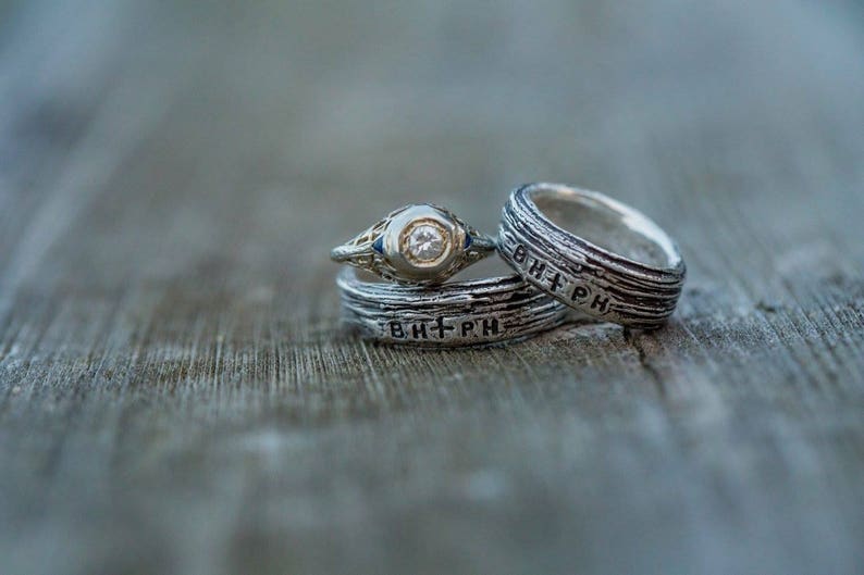 May include: Two silver wedding bands with a diamond engagement ring. The bands have the inscription "B+PH" on them.
