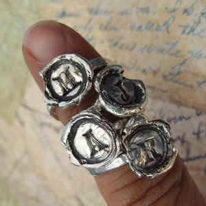 May include: Four silver rings with a wax seal design. Each ring features a different letter: H, J, A, and R.
