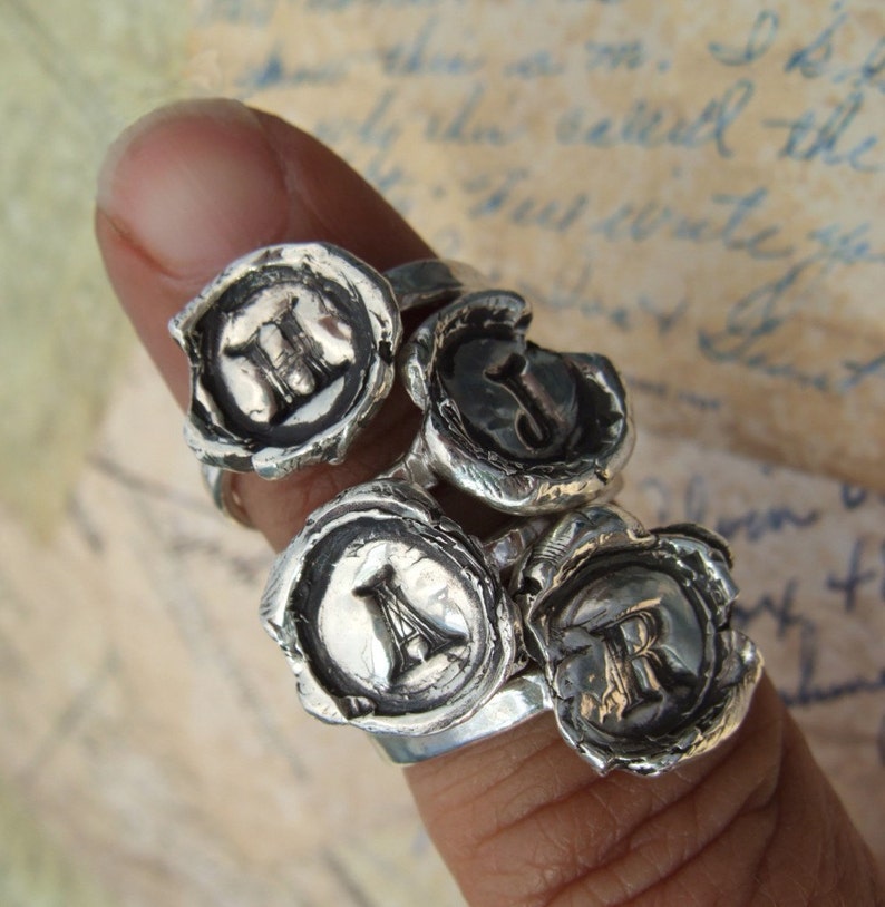 May include: Four silver rings with a wax seal design. Each ring features a different letter: H, J, A, and R.