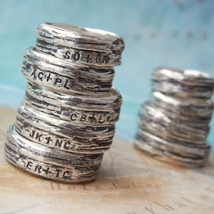 May include: A stack of silver rings with engraved initials and words, such as "SO+BR", "ACHPL", "CB+ER", "JK1+NC", and "ERT+TC".