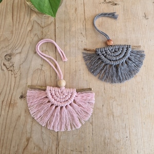 May include: Two handmade macrame wall hangings with wooden dowels and fringe. One is pink and the other is grey.
