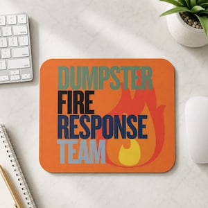 Może przedstawiać: Prostokątna podkładka pod mysz z pomarańczowym tłem i stylizowaną grafiką płomienia w kolorze czerwonym i ż&oacute;łtym. Napis DUMPSTER FIRE RESPONSE TEAM jest nadrukowany w ułożonych jedna pod drugą liniach w kolorach przygaszonej zieleni, czerni, ciemnego błękitu i jasnej szarości.