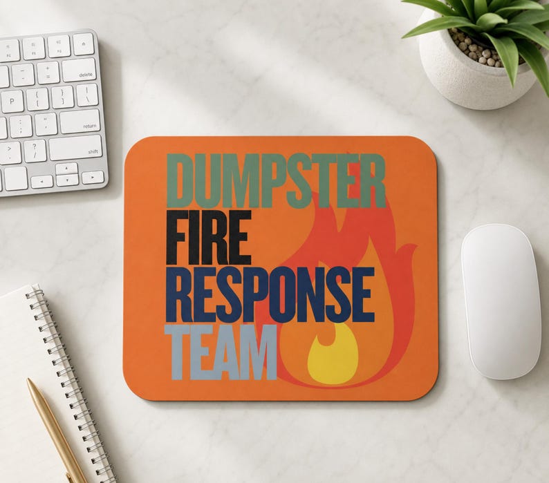 Może przedstawiać: Prostokątna podkładka pod mysz z pomarańczowym tłem i stylizowaną grafiką płomienia w kolorze czerwonym i ż&oacute;łtym. Napis DUMPSTER FIRE RESPONSE TEAM jest nadrukowany w ułożonych jedna pod drugą liniach w kolorach przygaszonej zieleni, czerni, ciemnego błękitu i jasnej szarości.