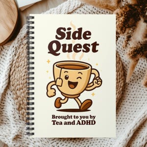 May include: A spiral-bound notebook with a cream-colored cover featuring a cartoon tea cup character with arms and legs. The text reads Side Quest at the top and Brought to you by Tea and ADHD at the bottom in dark brown, bold, rounded lettering.