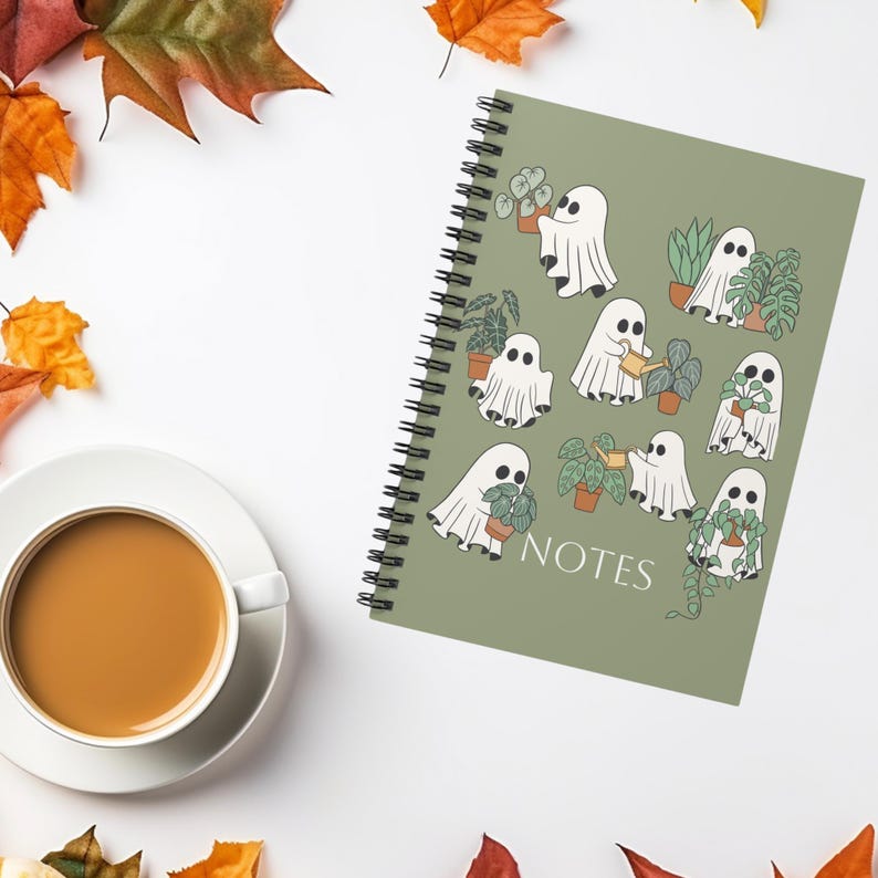 May include: A spiral-bound notebook with a sage green cover featuring a repeating pattern of white ghosts interacting with various potted houseplants. The word NOTES is printed in white at the bottom centre of the cover design.