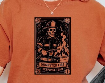 May include: Rust-colored sweatshirt featuring a graphic of a skeleton firefighter with a hose, flames, and the text "Dumpster Fire Response Team." The design is framed in a black border.