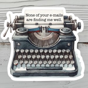 Op de afbeelding: Een donkergrijze vintage typemachine-sticker met een wit vel papier waarop de zwarte tekst staat: None of your e-mails are finding me well. De illustratie bevat gedetailleerde toetsen, een wagenretourhendel en een blauw inktlint.