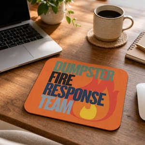 Może przedstawiać: Prostokątna podkładka pod mysz z pomarańczowym tłem i stylizowaną grafiką płomienia w kolorze czerwonym i ż&oacute;łtym. Napis DUMPSTER FIRE RESPONSE TEAM jest nadrukowany w ułożonych liniach bezszeryfową czcionką w kolorach morskim, czarnym, granatowym i jasnoniebieskim.