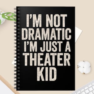 May include: A black spiral-bound notebook with the text "I'M NOT DRAMATIC I'M JUST A THEATER KID" in distressed white lettering. The notebook is open, and the text is centered on the cover.