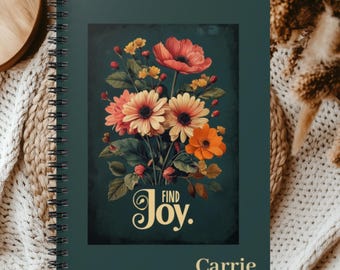 May include: A dark green spiral-bound notebook featuring a central rectangular illustration of a colorful floral bouquet with red, orange, and yellow flowers. The text "FIND Joy." is printed in gold above the name "Carrie" in gold lettering.