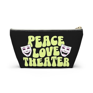 May include: Black zippered pouch with the words "PEACE LOVE THEATER" in light green, along with two theater masks. The pouch has a gold zipper and a white interior. The design is centered on the front of the pouch.