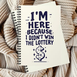 May include: A spiral-bound notebook with a cream-colored cover featuring dark blue text that reads I'M HERE BECAUSE I DIDN'T WIN THE LOTTERY, accompanied by a stylized dollar sign symbol surrounded by small four-pointed star accents.