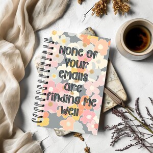 Może przedstawiać: Szary notes spiralny z kwiatowym wzorem i tekstem "None of your emails are finding me well".