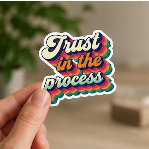 May include: A die-cut sticker featuring the text Trust in the process in a bold, retro-inspired font. The lettering displays a multi-layered, stacked effect with a vibrant color palette of cream, orange, pink, purple, and teal, creating a shadow.