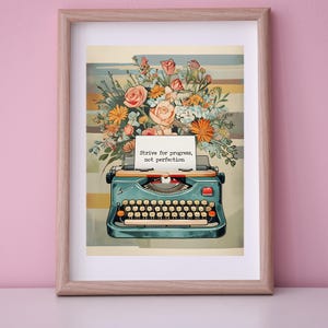 Puede incluir: Una máquina de escribir vintage con un ramo de flores en la parte superior. La máquina de escribir tiene un cuerpo azul y un papel blanco con el texto "Strive for progress, not perfection".