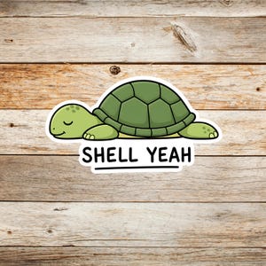 May include: A die-cut sticker featuring a cartoon turtle with a light green head and a dark green shell. The turtle has closed eyes and a small smile. Below the turtle, the text SHELL YEAH is printed in black capital letters with a line underneath.