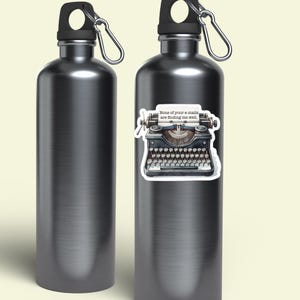 Op de afbeelding: Twee metallic grijze waterflessen met zwarte doppen en zilveren karabijnhaken. E&eacute;n fles heeft een sticker van een vintage typemachine met een vel papier waarop staat: "None of your e-mails are finding me well." De flessen hebben een gladde afwerking.
