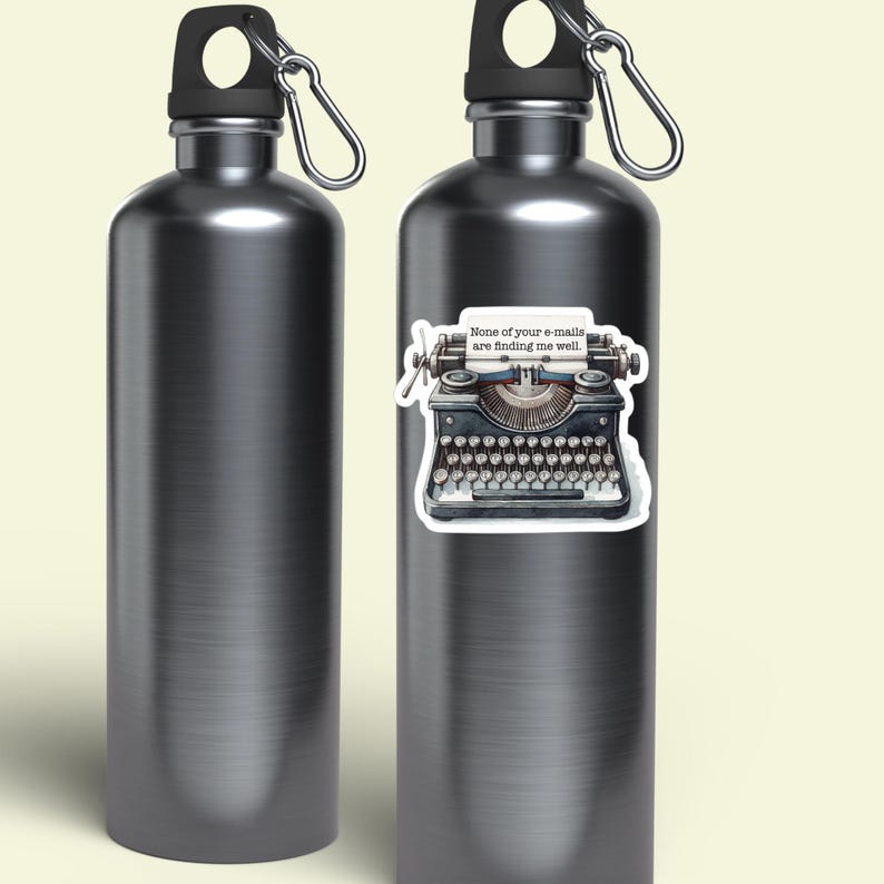 Op de afbeelding: Twee metallic grijze waterflessen met zwarte doppen en zilveren karabijnhaken. E&eacute;n fles heeft een sticker van een vintage typemachine met een vel papier waarop staat: "None of your e-mails are finding me well." De flessen hebben een gladde afwerking.