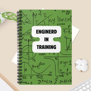 May include: A green spiral notebook with a white cover that says "Enginerd in Training". The cover is decorated with handwritten mathematical equations and formulas.