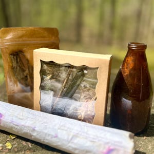 Puede incluir: Un conjunto de tres artículos para manualidades o herboristería, que incluye una caja de plástico transparente con flores y ramitas secas, una bolsa de papel marrón con hierbas secas y una botella de vidrio marrón.