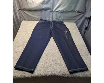 May include: Dark blue denim cargo pants with white stitching. The pants have a classic five-pocket design, a cargo pocket on the right leg, and a button and zipper closure. The pants are laid flat on a textured surface.