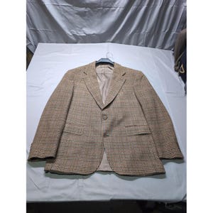 May include: A brown and tan houndstooth blazer with a two-button closure, notched lapels, and two front pockets. The blazer is hanging on a black hanger against a white background. The interior lining is a solid tan color.