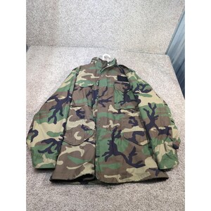 May include: Camouflage pattern military jacket with a button-up front, four front pockets, and a collar. The jacket features a green, brown, and black woodland camouflage design. The jacket is made of a durable material.