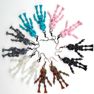 May include: A set of ten skeleton earrings in various colors, including black, white, turquoise, pink, and brown. The earrings are made of polymer clay and feature a dangling skeleton design.