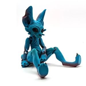 May include: A blue and purple articulated cat figurine with large ears and a long tail. The cat is sitting with its legs outstretched.
