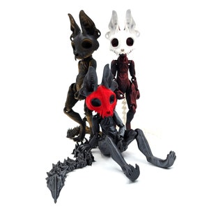 May include: Three articulated skeletal figures with animal-like features. The figures are made of black, white, and red plastic. The figures have a skull-like head with large eyes and a long, thin tail.
