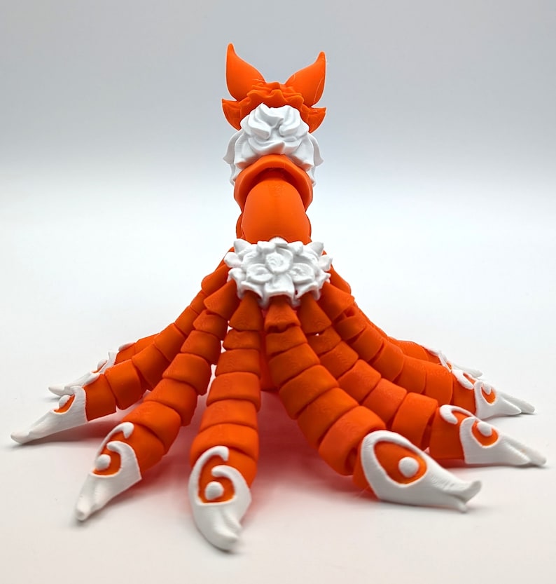 Peut inclure: Figurines orange et blanche d'une cr&eacute;ature &agrave; plusieurs bras et une queue. La cr&eacute;ature a un collier blanc et un motif floral blanc autour de la taille. La figurine est en plastique et a une finition lisse.
