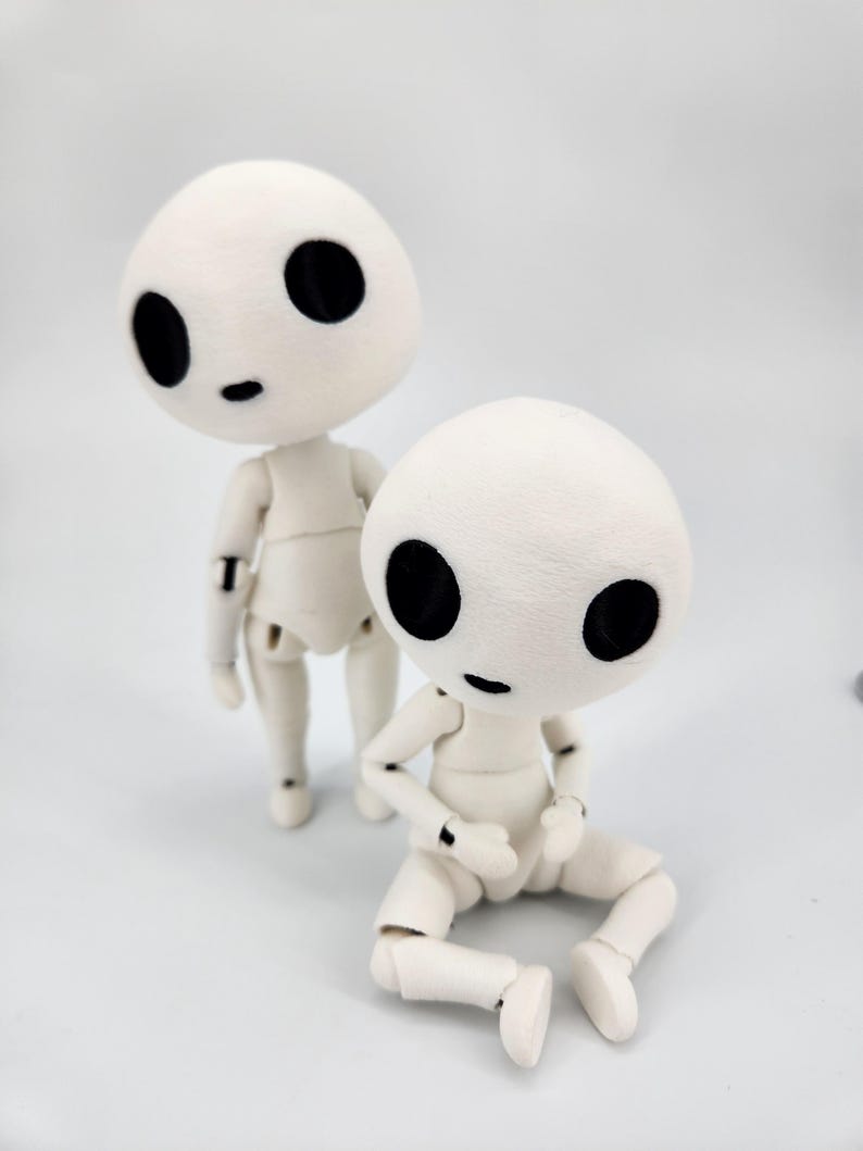 May include: Two white articulated dolls with large black eyes and small black mouths. One doll is standing, the other is sitting with its legs bent. The dolls have a soft, textured appearance and are reminiscent of characters from a fantasy film.