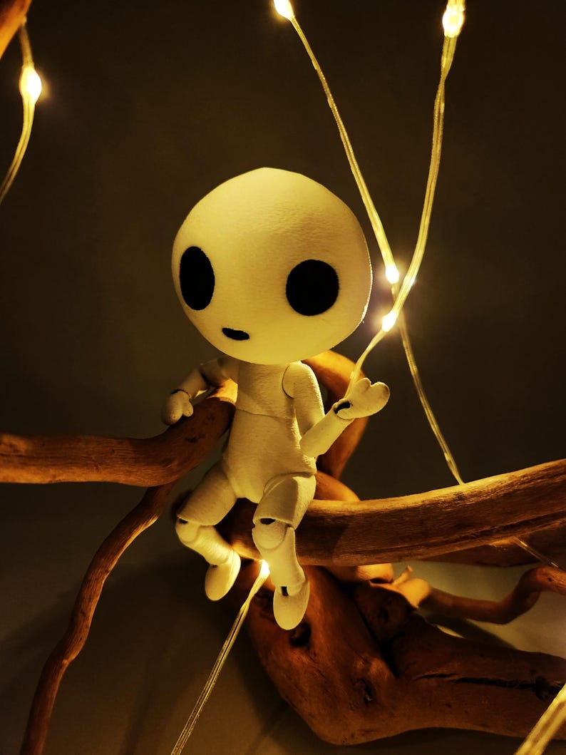 May include: A white, articulated doll with large black eyes and a small mouth sits on a brown branch. The doll is illuminated by small, warm-toned fairy lights, creating a whimsical and enchanting scene. The doll's pose suggests a sense of curiosity.