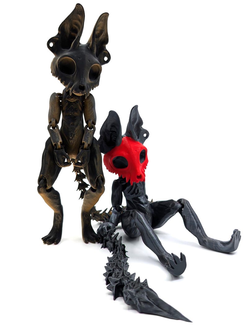 May include: Two articulated black and gold skeletal figures with long tails. The figure on the left is standing and the figure on the right is sitting with its tail extended behind it. The figure on the right has a red skull face.
