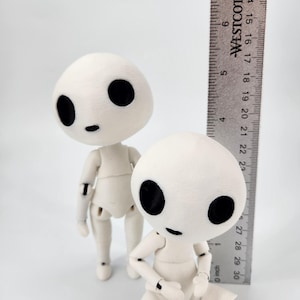 May include: Two off-white articulated dolls with large black eyes and small mouths. A ruler is placed next to the dolls, measuring approximately 7 inches. The dolls have a minimalist design and are posed in different positions.