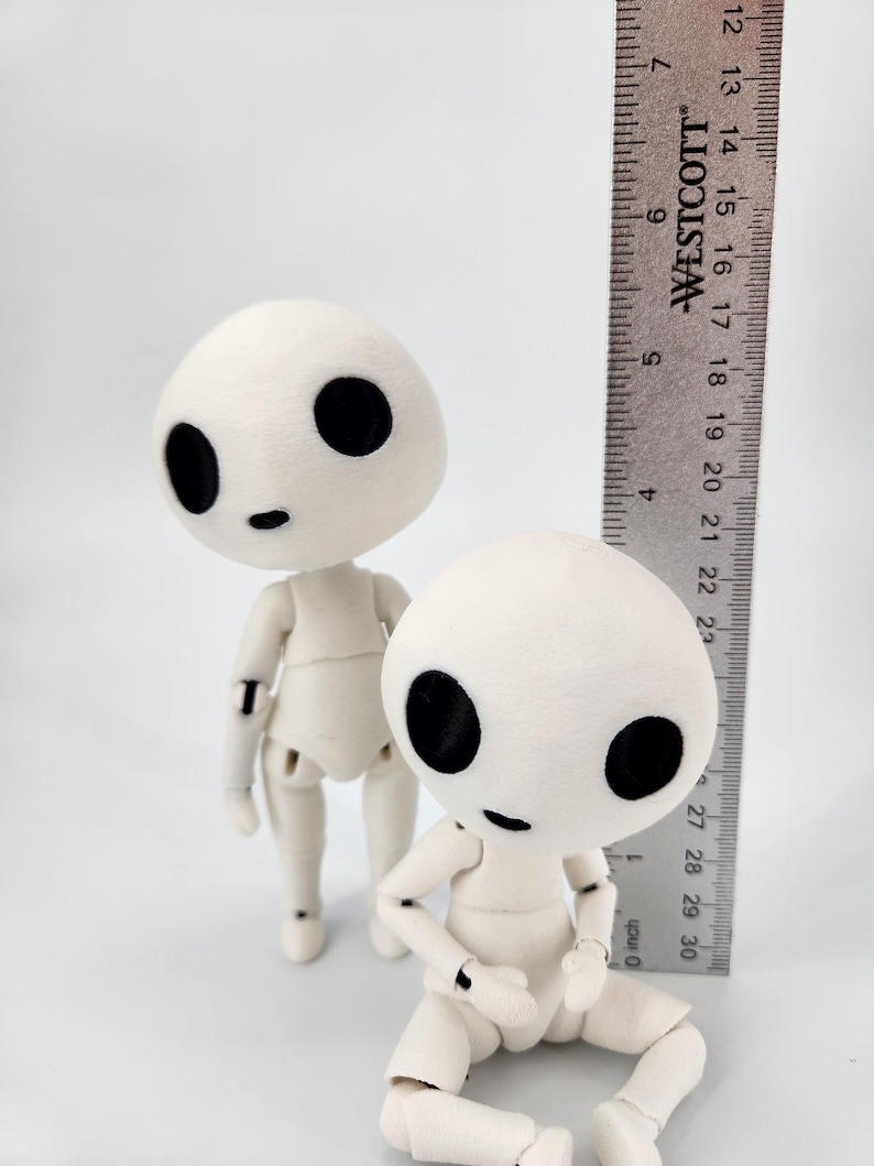May include: Two off-white articulated dolls with large black eyes and small mouths. A ruler is placed next to the dolls, measuring approximately 7 inches. The dolls have a minimalist design and are posed in different positions.