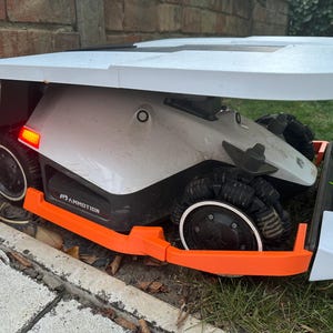 以下が含まれることがあります： 白とオレンジのアクセントが付いたロボット芝刈り機。芝刈り機は、黒いトレッドと黒いベースを備えた4つの車輪を備えています。芝生の上に置かれています。