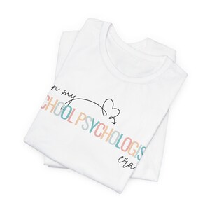 May include: White t-shirt with the text "In my School Psychologist era" in rainbow colors with a heart drawn next to it.